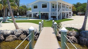 Propiedad frente al mar de dos pisos con una terraza de madera que conduce a una zona de piscina.