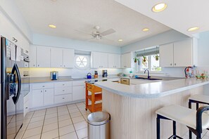 A modern kitchen with white cabinets, a central island, a ceiling fan, and a window with a view. - Luxurious waterfront home with panoramic views, pool, spa, & dock (Marathon)