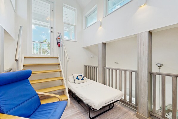 Een kamer met een bed, een blauwe stoel, een trap en uitzicht op het buiten.