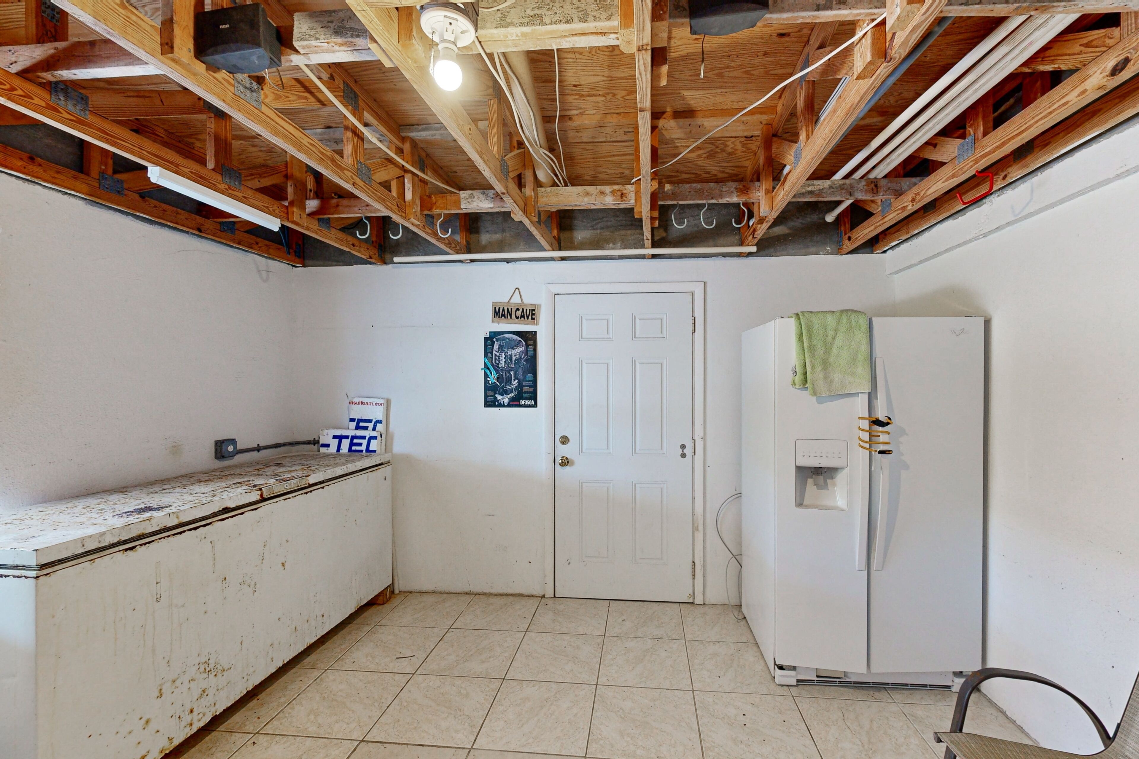 A room with exposed wooden beams, a white door, a white refrigerator, and a tiled floor.
