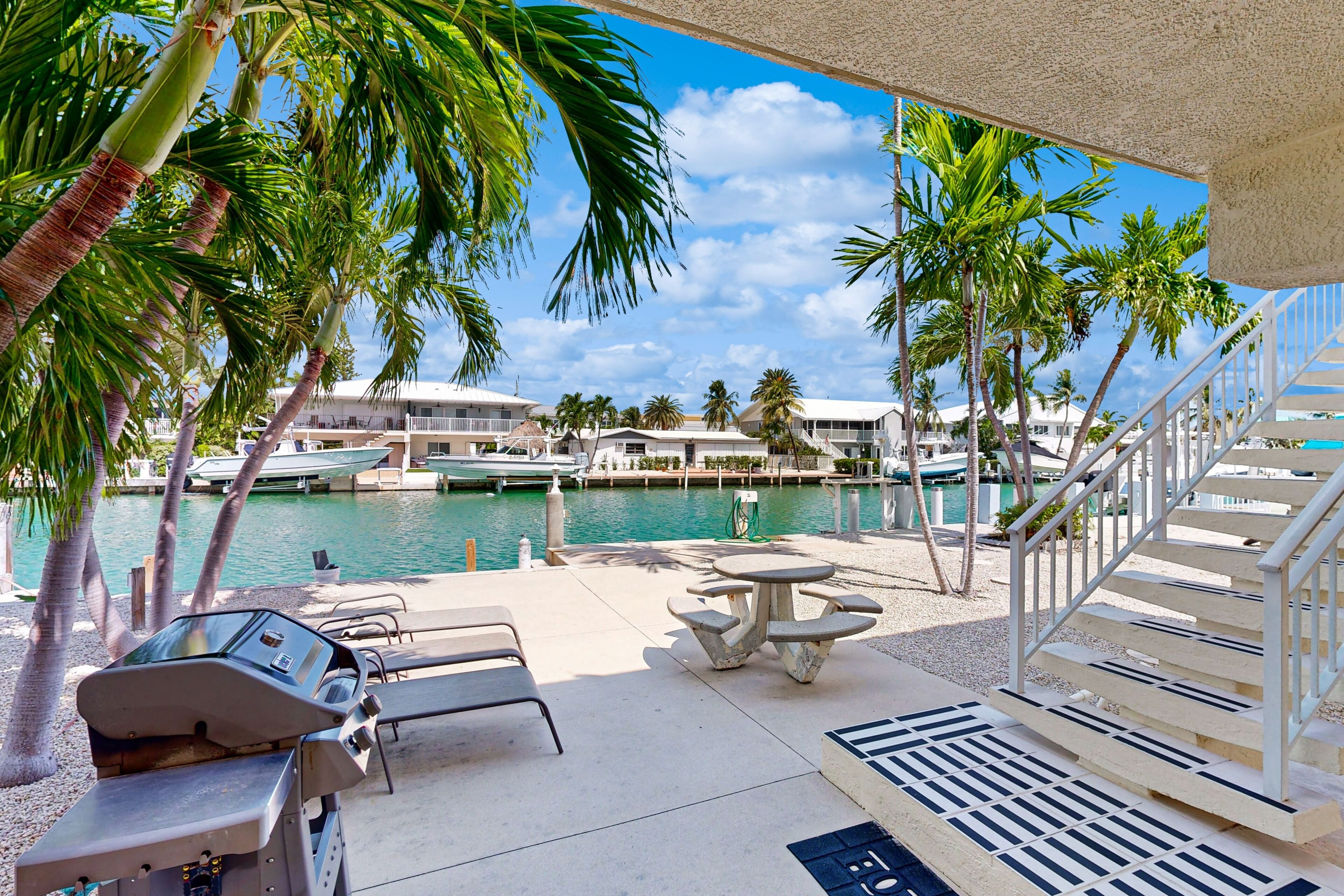 A poolside area with lounge chairs, a grill, and a view of the marina.