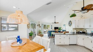 Une cuisine spacieuse avec des meubles blancs, une table à manger en bois et un ventilateur de plafond.