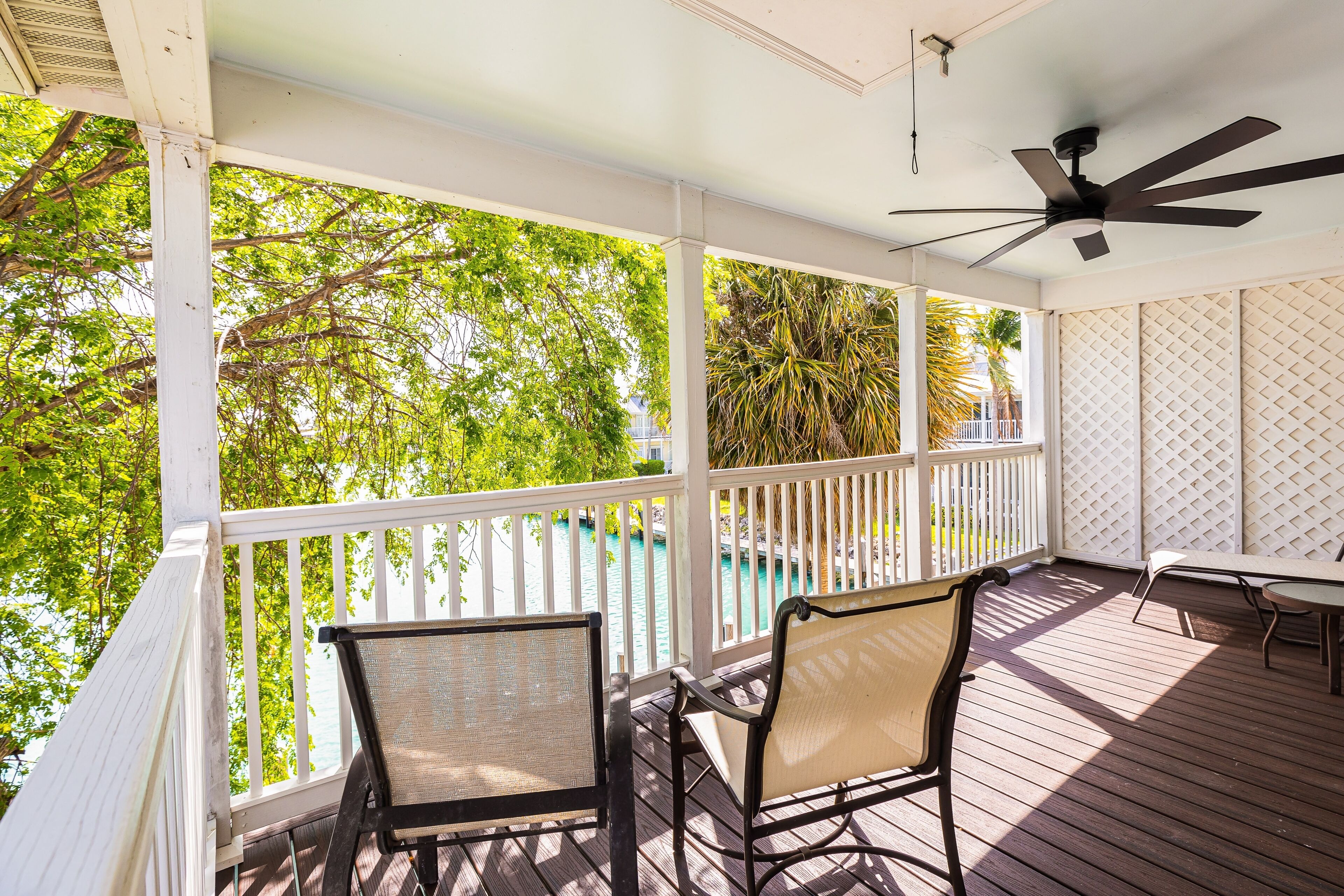A covered outdoor area with a wooden deck, white railings, and a ceiling fan.