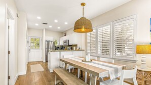 A modern kitchen with white cabinets, a wooden dining table, and a hanging pendant light. - Waterfront, dog-friendly home with beautiful canal view & 2 shaded porches (Duck Key)