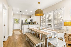 A modern kitchen with white cabinets, a wooden dining table, and a hanging pendant light. - Waterfront, dog-friendly home with beautiful canal view & 2 shaded porches (Duck Key)