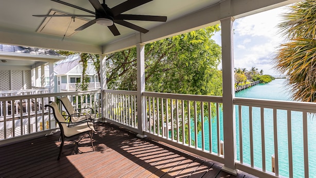 A covered outdoor area with a ceiling fan, a wooden deck, a white railing, and a view of a turquoise body of water. - Waterfront, dog-friendly home with beautiful canal view & 2 shaded porches (Duck Key)