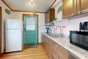 A kitchen with wooden cabinets, a stainless steel sink, a microwave, and a teal door. - Bright Condo with Homey Feel, Entertainment & Private Parking - Beach Nearby (Key West)