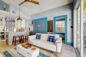 A modern kitchen with a central island, a white sofa with patterned cushions, and a wooden ceiling fan. - Bright Duplex with Private Heated Pool, Central AC, WiFi, & Private Washer/Dryer (Key West)