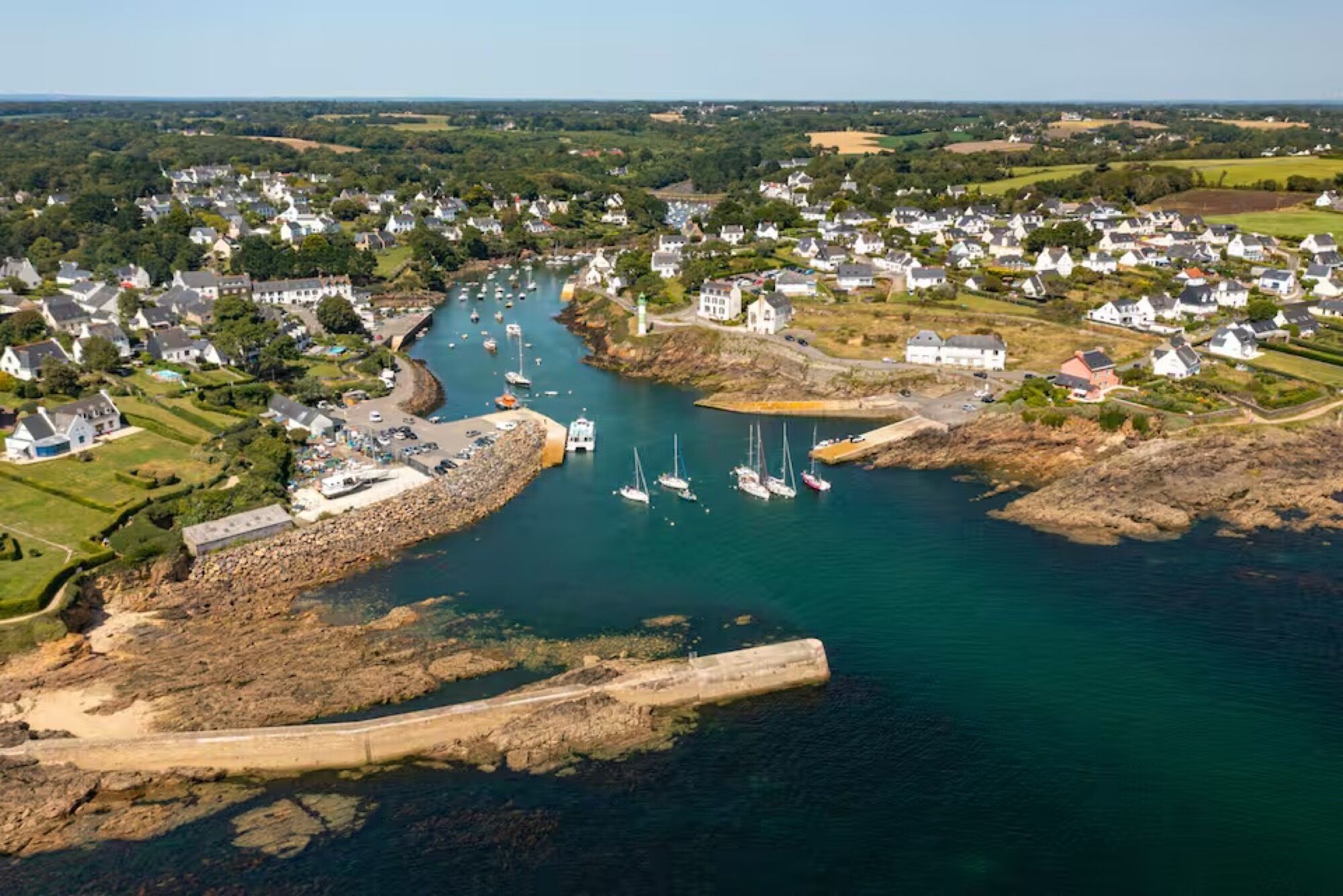 An aerial view of a coastal town with houses, a marina, and a rocky shoreline.