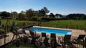 A rectangular swimming pool with a wooden deck and lounge chairs.