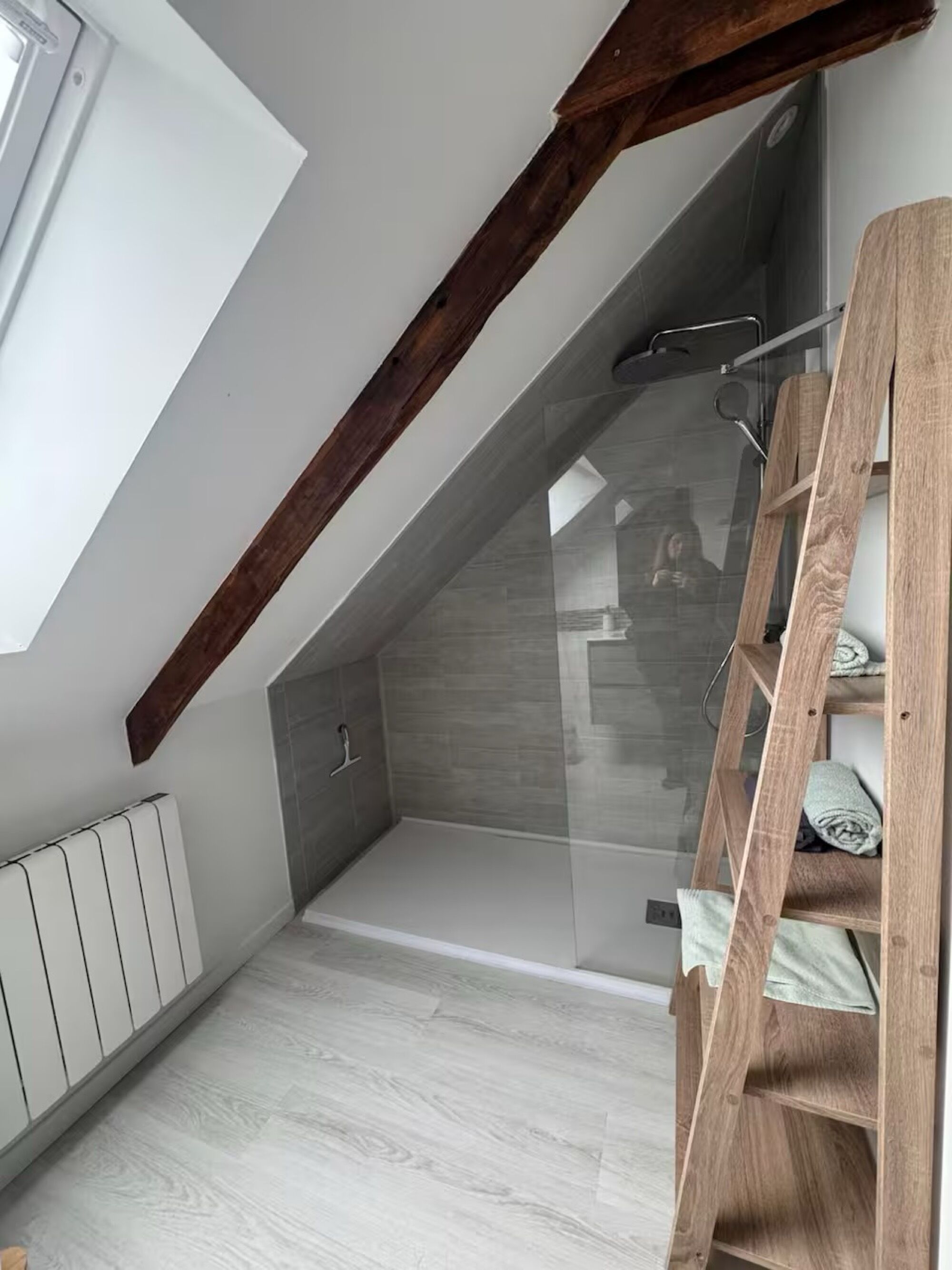 Una habitación con techo inclinado, una escalera de madera, un radiador y una zona de ducha.