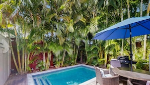 Ein Garten mit Swimmingpool, Korbmöbeln und Grill.