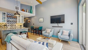 Ein modernes Wohnzimmer mit einer Couch, zwei Sesseln, einem Couchtisch und einem an der Wand montierten Fernseher.