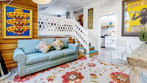 Uma sala de estar moderna com um sofá azul claro, almofadas coloridas, um tapete floral e uma escada com corrimão branco.