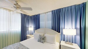 A hotel room with a bed, two bedside tables, a ceiling fan, and blue curtains. - Cozy Dog-Friendly Condo w/ Shared Pool, Hot Tub, Private Deck & Parking (Key West)