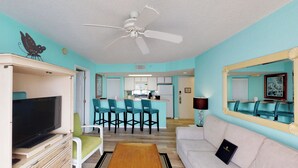 A living room with a television, a white sofa, a wooden coffee table, and a ceiling fan. - Cozy Dog-Friendly Condo w/ Shared Pool, Hot Tub, Private Deck & Parking (Key West)