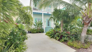 Um edifício de dois andares com varanda, rodeado por plantas tropicais exuberantes e um caminho de concreto.