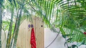Uma porta de madeira com uma toalha vermelha pendurada, cercada por folhagem verde exuberante.