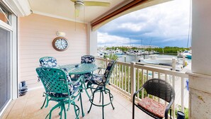 Een balkon met een tafel en stoelen, een plafondventilator, een klok en uitzicht op een jachthaven met boten.
