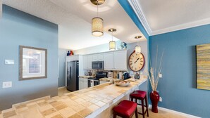 Een moderne keuken met een groot eiland, witte kasten en een rode vaas met decoratieve takken.