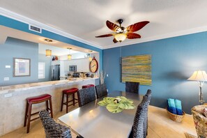A modern dining area with a large table, red bar stools, and a ceiling fan. - Dog-friendly, Gulf-front condo with pool, hot tub & gorgeous sunset views (Key West)
