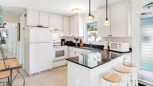 Cozinha moderna com armários brancos, uma ilha central com banquetas, micro-ondas e pia.