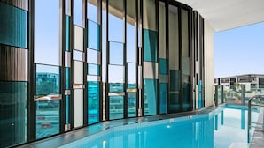 A modern indoor swimming pool with large windows, a clear view of the outside, and a tiled floor.