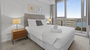 A hotel room with a large bed, two bedside tables, a view of the city, and a window.