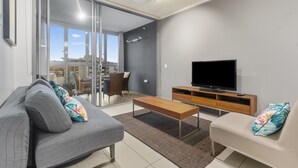 A modern living room with a sofa, a coffee table, a TV, and a sliding glass door leading to a balcony.