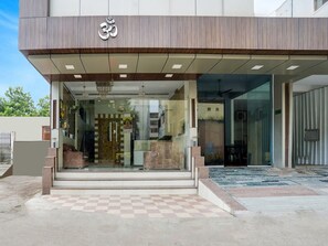 Un edificio moderno con un llamativo símbolo 'Om' sobre la entrada, fachada de vidrio y un diseño de baldosas de ajedrez en la entrada.