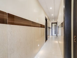 Un pasillo moderno con suelo de mármol, detalles de paneles de madera y una puerta con marco oscuro.