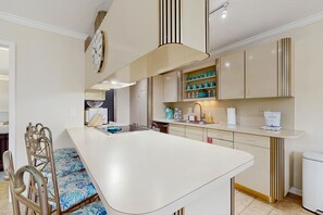 A modern kitchen with a central island, a dining area with a metal chair, and a built-in clock on the wall. - Oceanside condo with heated pool, tennis courts & great location (Marathon)