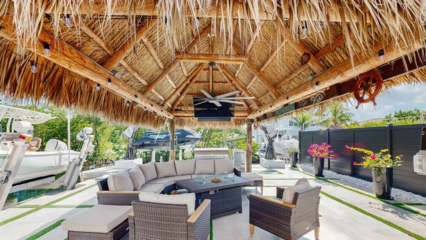 Un espace extérieur aménagé en terrasse, doté d’un toit de chaume, d’un grand canapé, de meubles en osier et d’un bateau amarré à proximité.