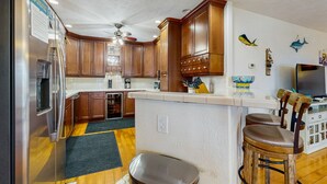 Cozinha compacta com armários de madeira, geladeira, micro-ondas e uma pequena ilha com banquetas.