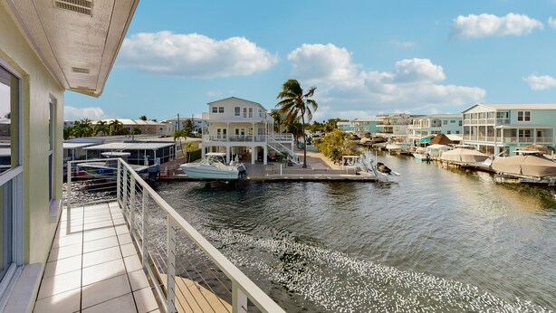 Ein Anwesen am Wasser mit einem Balkon mit Blick auf eine Marina, wo Boote vor Anker liegen, und Häuser im Hintergrund.