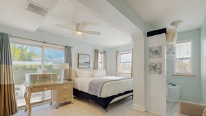 Ein Schlafzimmer mit einem Bett, einem Schminktisch, einem Deckenventilator und einem Fenster mit Vorhängen.