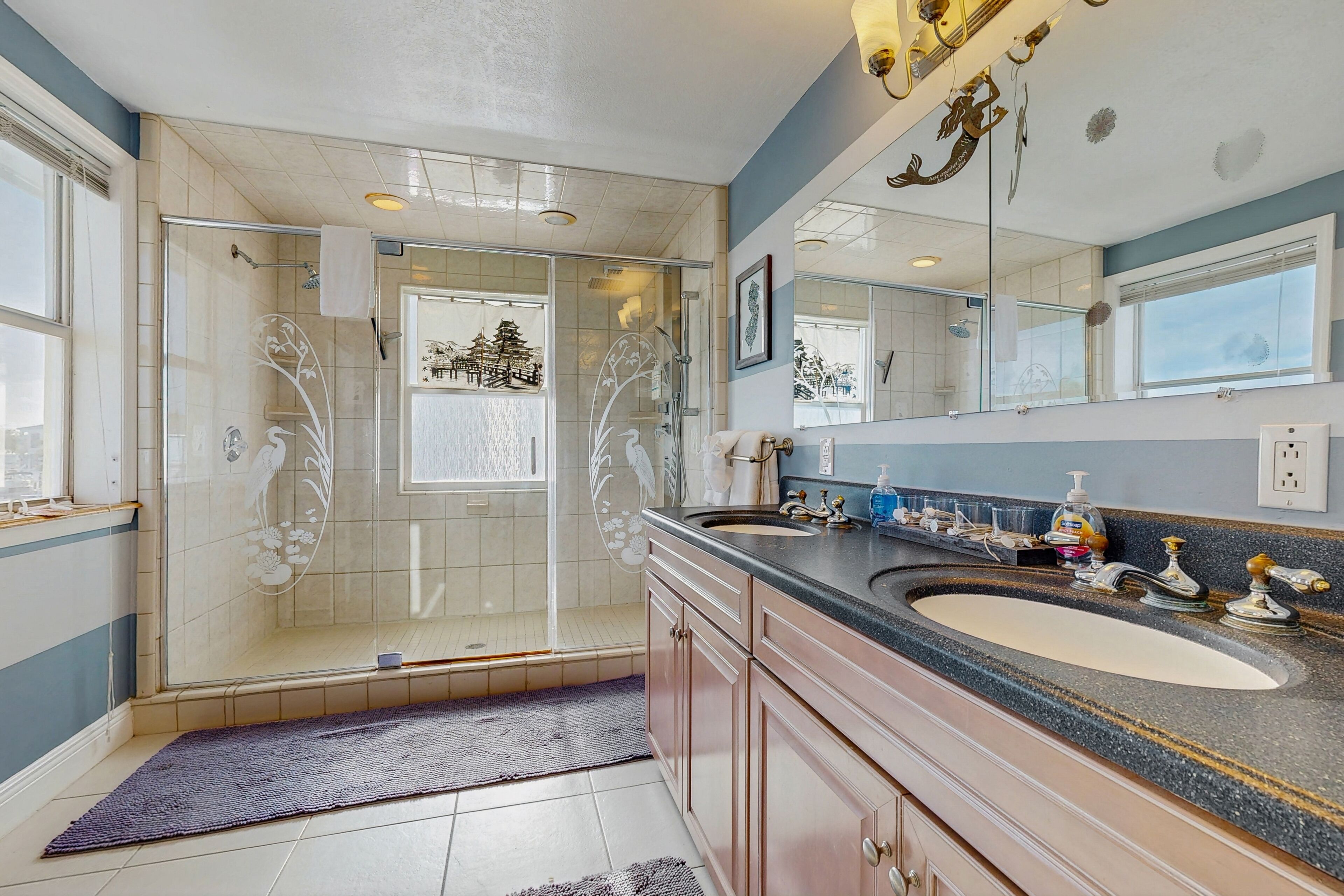 A modern bathroom with a glass-enclosed shower, a large vanity with dual sinks, and a mirror with decorative elements.