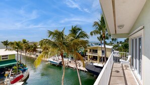 A balcony overlooking a marina with boats docked, palm trees, and a clear blue sky. - Oceanfront, Snowbird-Friendly Home with High-Speed WiFi, Ocean Views, and Dock (Key Largo)