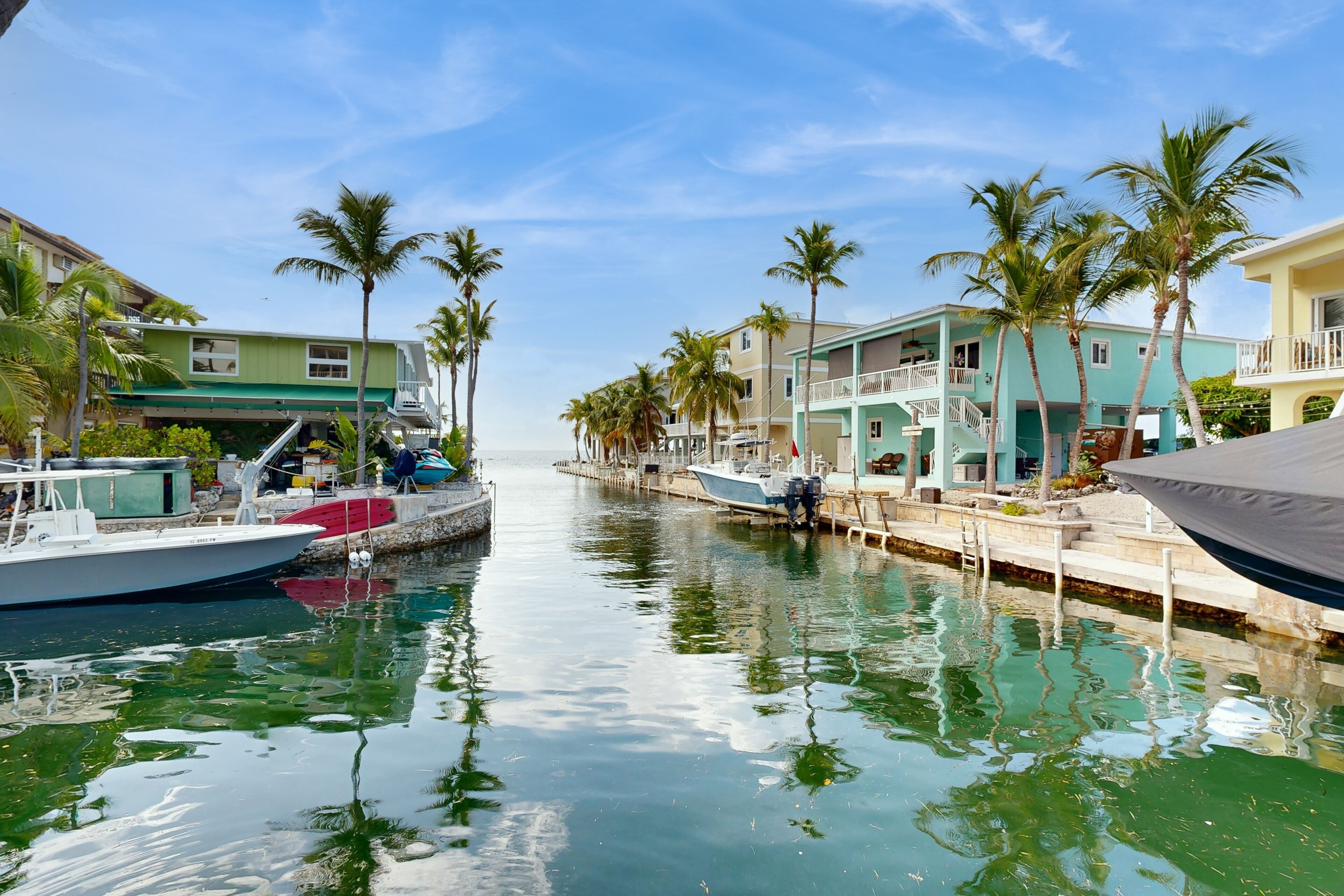 A marina with boats docked along a waterway, surrounded by buildings with balconies and palm trees.
