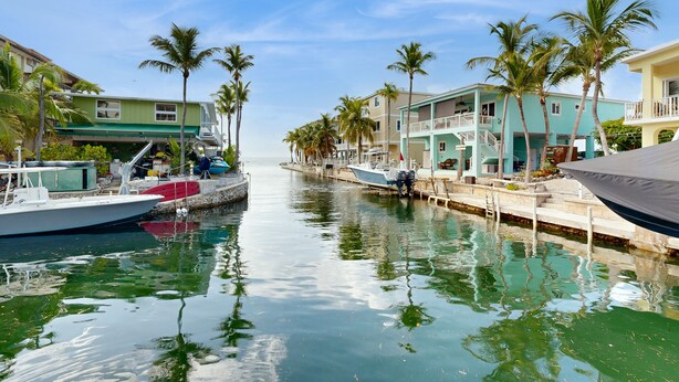 A marina with boats docked along a waterway, surrounded by buildings with balconies and palm trees. - Oceanfront, Snowbird-Friendly Home with High-Speed WiFi, Ocean Views, and Dock (Key Largo)