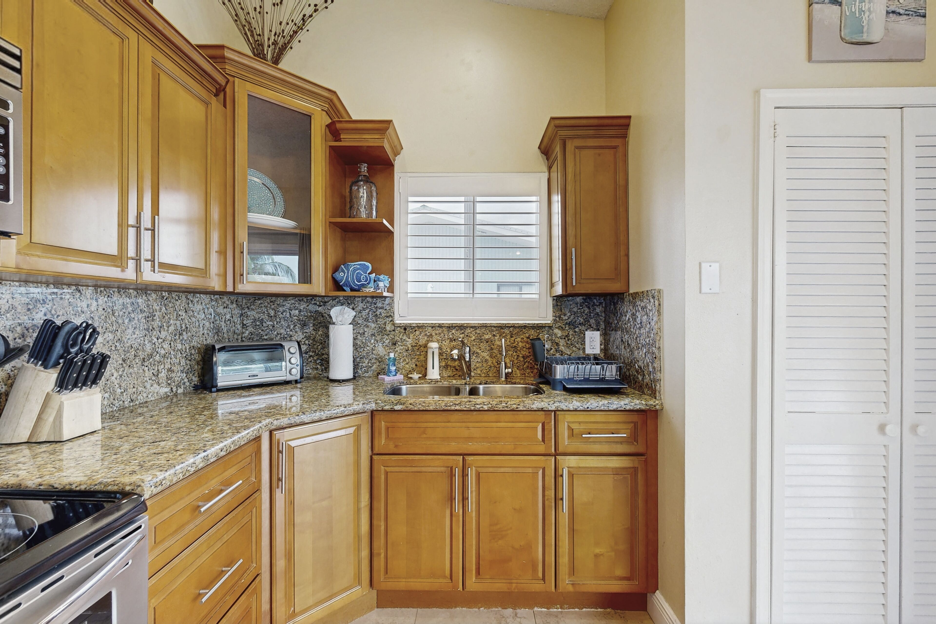 A kitchen with wooden cabinets, granite countertops, a stove, a sink, and a window with blinds.