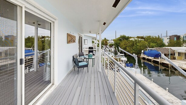 A balcony with a view of the water, a table with chairs, and a railing. - Spacious canal-front home with balcony - monthly rental (Key Largo)