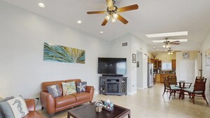 A spacious living room with a brown leather sofa, a coffee table, and a flat-screen TV. There is a dining area with a table and chairs, and a kitchen in the background. - Spacious canal-front home with balcony - monthly rental (Key Largo)