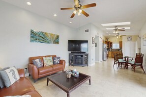 A spacious living room with a brown leather sofa, a coffee table, and a flat-screen TV. There is a dining area with a table and chairs, and a kitchen in the background. - Spacious canal-front home with balcony - monthly rental (Key Largo)