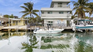 A marina with a white boat docked in the water, a multi-story building with balconies, and palm trees in the background. - Spacious canal-front home with balcony - monthly rental (Key Largo)