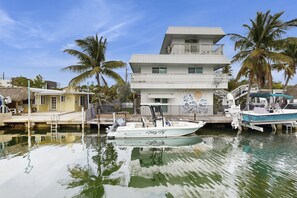 A marina with a white boat docked in the water, a multi-story building with balconies, and palm trees in the background. - Spacious canal-front home with balcony - monthly rental (Key Largo)
