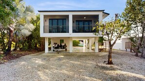 Een modern huis met twee verdiepingen, een overdekt terras, een grindpad en tropische beplanting eromheen.