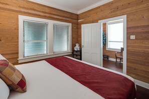 A bedroom with wooden paneling, a bed with a red runner, and a door leading to another room.