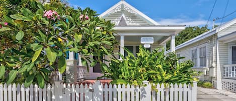 A historic inn with a white facade, a covered porch, and lush tropical foliage.