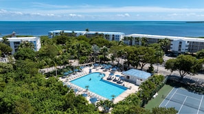 A resort with a swimming pool surrounded by lounge chairs and umbrellas, a tennis court, and a view of the ocean. - Coastal retreat with private balcony, pool, & easy beach access (Tavernier)